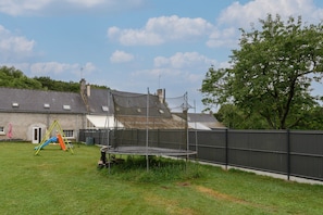 Ein Wohnhausgarten mit Trampolin, Schaukel und umzäunter Fläche.