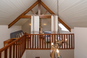 Un dormitorio tipo loft con techo inclinado, vigas de madera, cama con ropa de cama estampada, mesita de noche y lámpara colgante.