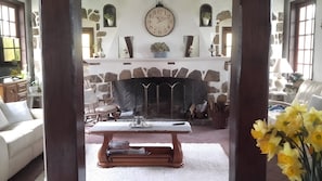 A room with a stone fireplace, a clock, and a table with a vase of flowers.