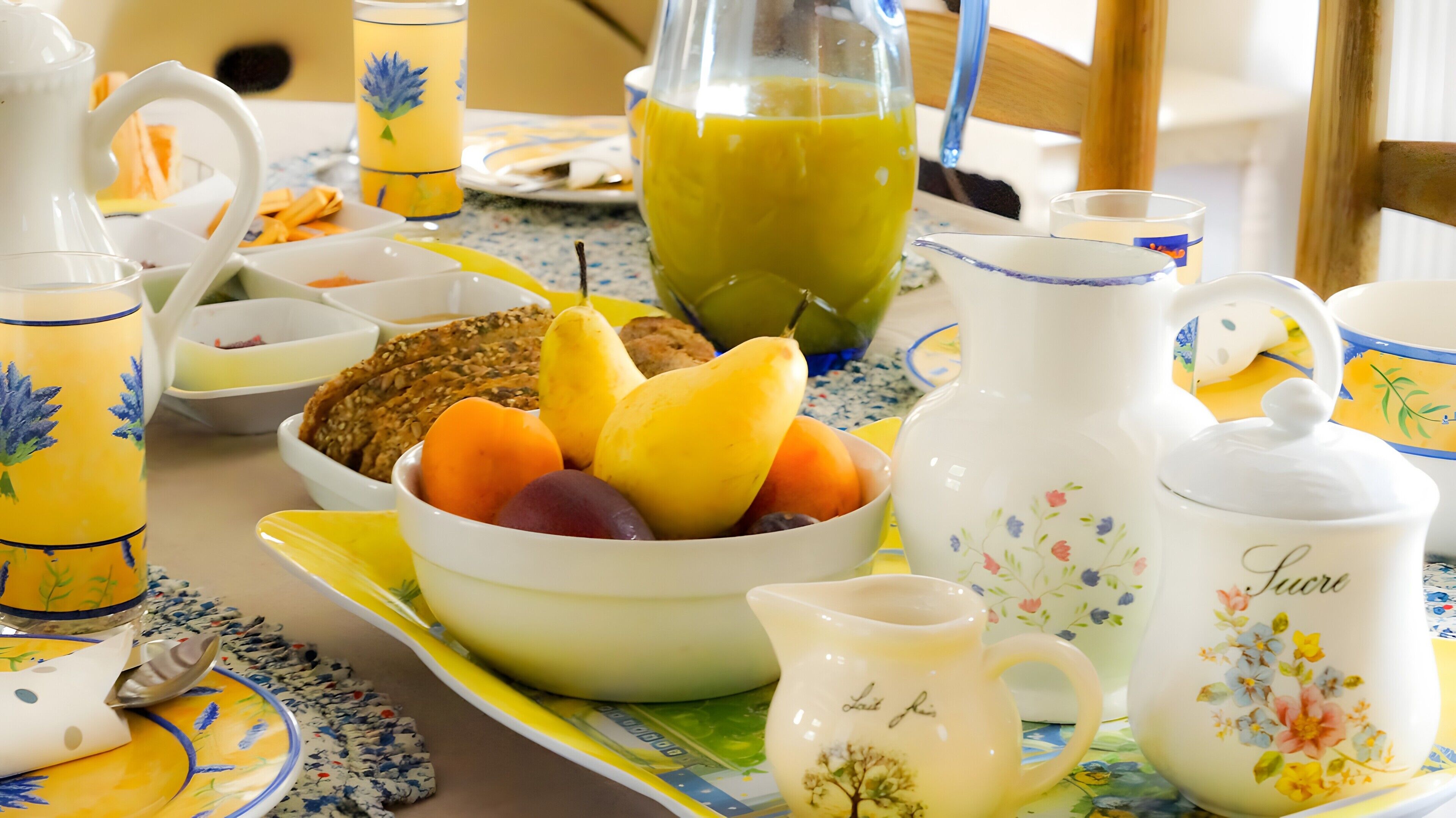 Een ontbijtsetting met een fruitschaal, een kan sap en diverse ontbijtartikelen op een tafel.