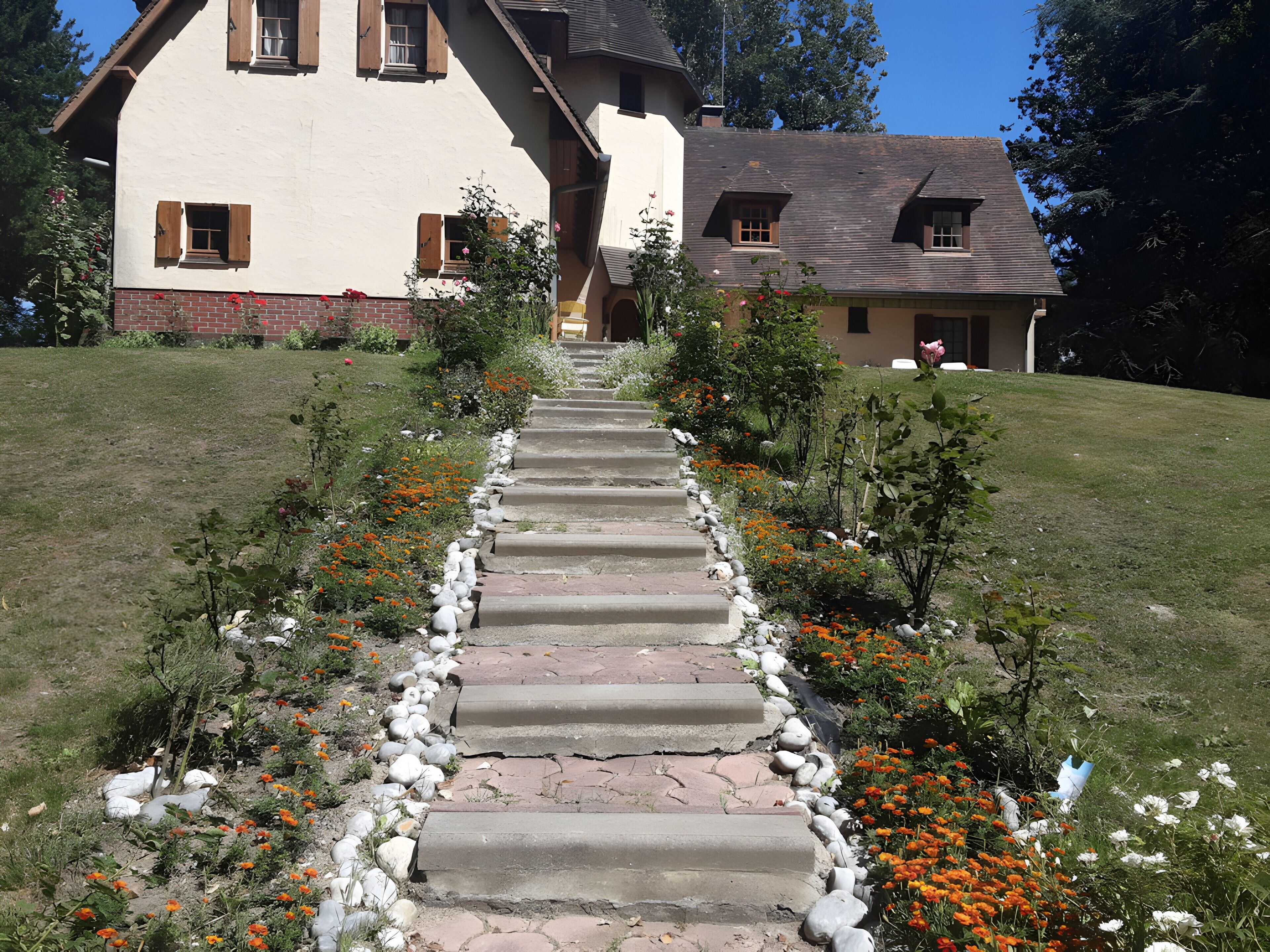 Un chemin de pierres mène à une maison dotée d’un toit en pente et de volets en bois.