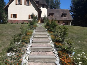 A stone pathway leading to a house with a sloped roof and wooden shutters.