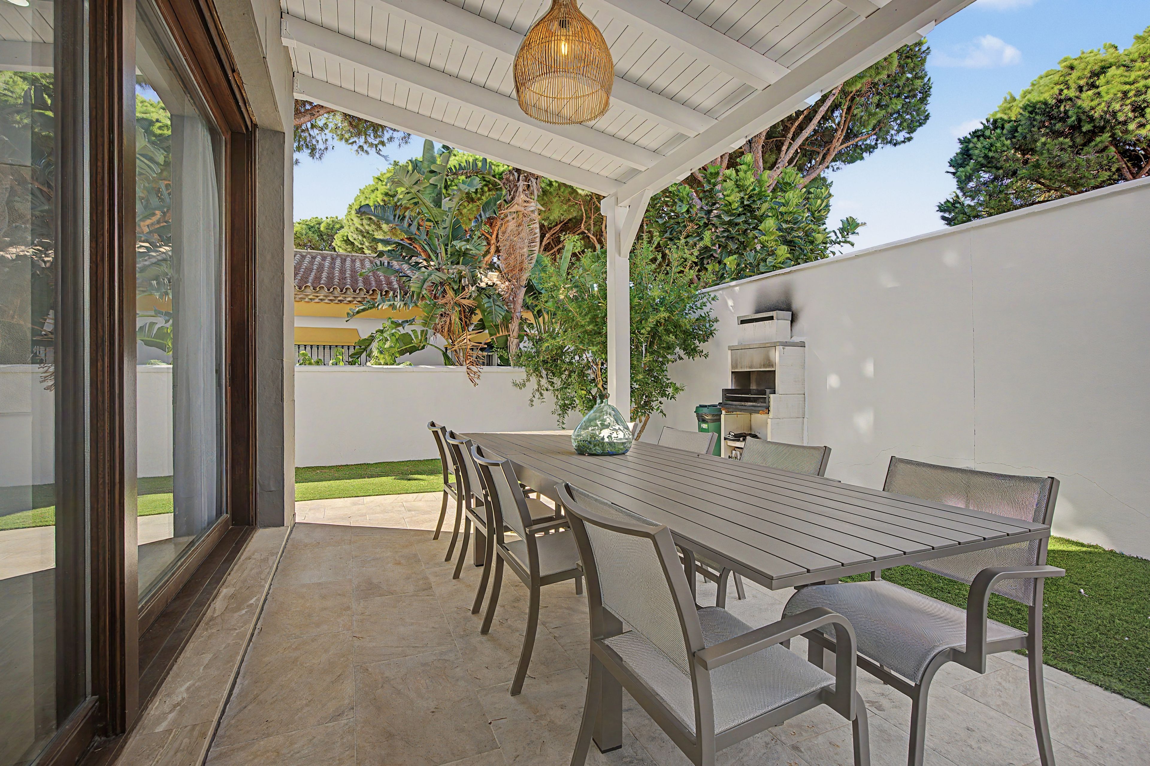 Un patio exterior con una mesa y sillas para comer, rodeado por un muro blanco y follaje.