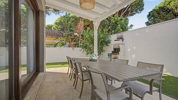 Un patio exterior con una mesa y sillas para comer, rodeado por un muro blanco y follaje.