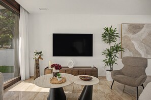 Een moderne woonkamer met een grote flatscreen televisie aan de muur, een comfortabele fauteuil, een ronde salontafel en een potplant.