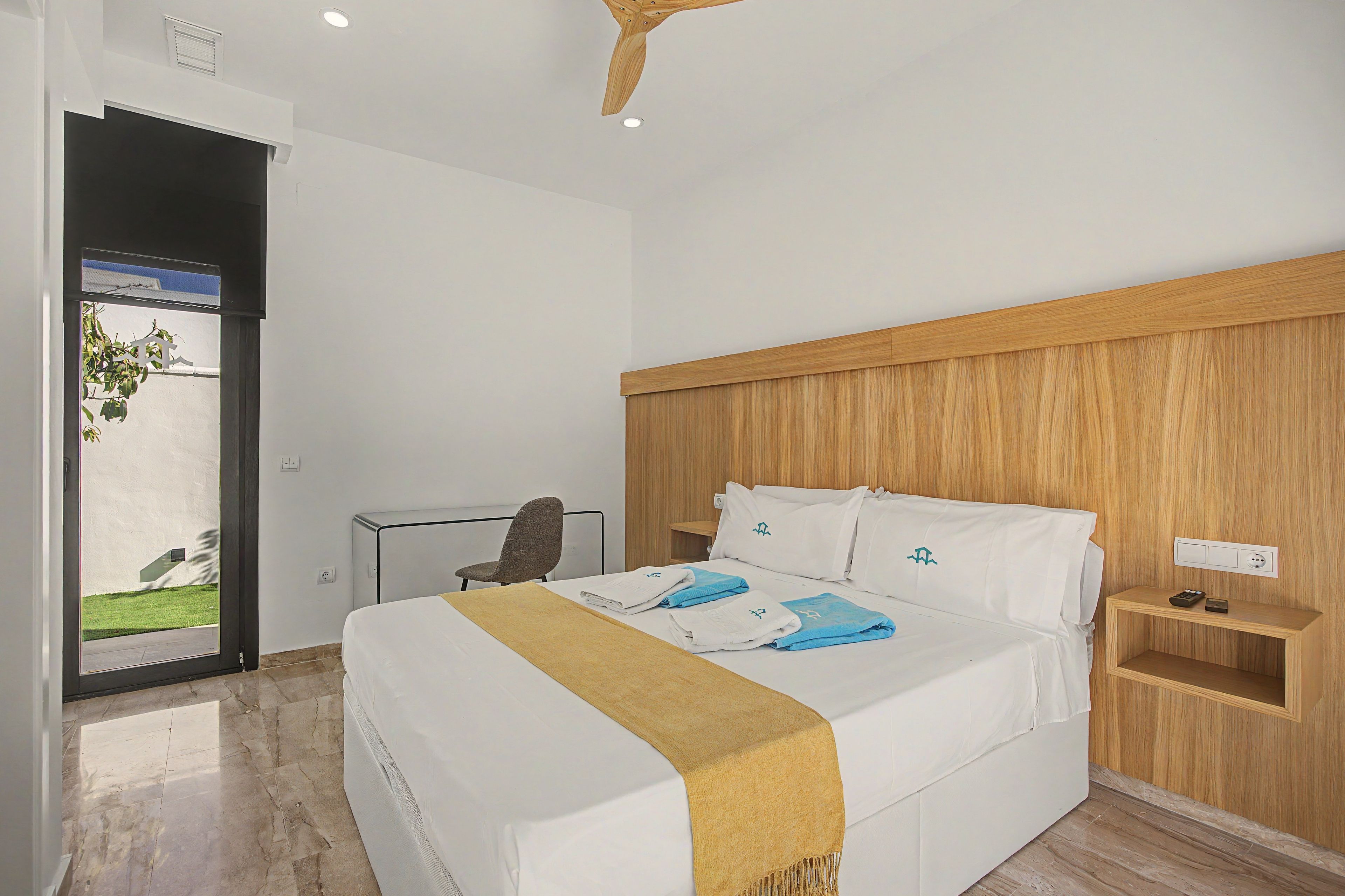 Habitación de hotel con una cama, un escritorio, una silla y cabecera de madera.