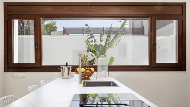 Eine Küche mit einem großen Fenster, einer weißen Arbeitsplatte, einem Spülbecken und einer Vase mit Früchten.