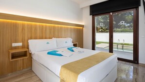 Ein modernes Hotelzimmer mit einem großen Bett, einem hölzernen Kopfteil, einem kleinen Nachttisch und Blick auf einen Swimmingpool durch eine Glastür.