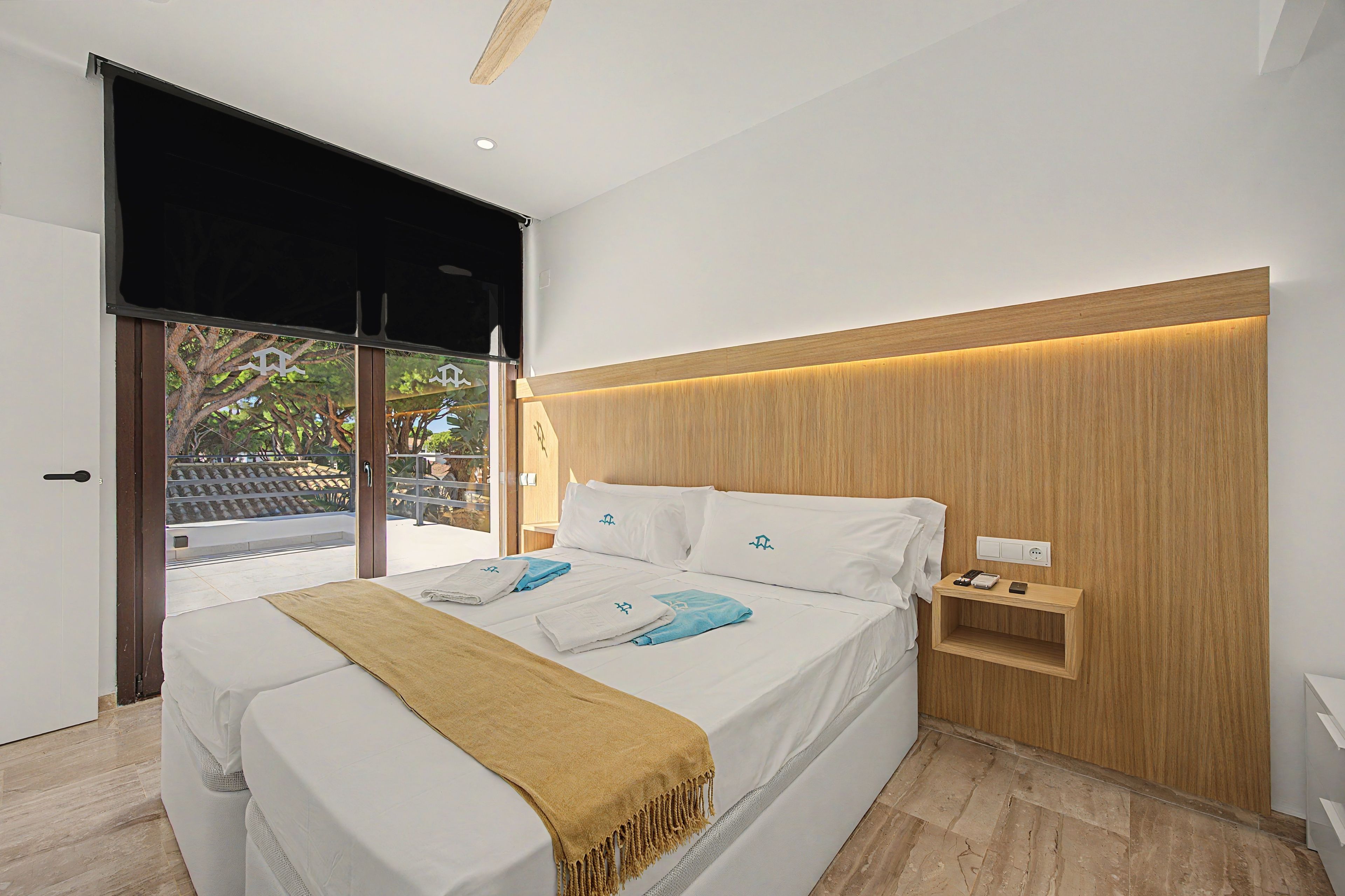 Un dormitorio moderno con cama, mesita de noche, toma de corriente y vistas al exterior.