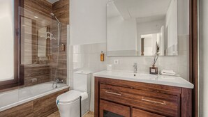 Un bagno moderno con doccia vetro, water bianco, mobile bagno in legno con specchio e lavandino.