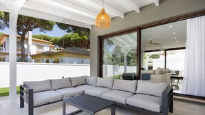 Ein moderner Außenbereich mit Ecksofa, Couchtisch, großen Schiebegläsern und Blick auf ein traditionelles Gebäude.