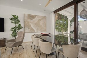 Un comedor moderno con una mesa de vidrio, seis sillas, un cuadro abstracto grande y una planta en maceta.