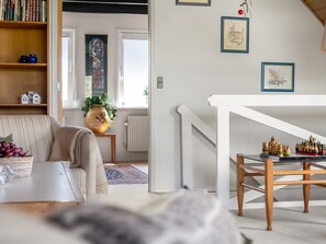 Ein Wohnzimmer mit einer Couch, einem Couchtisch, einem Bücherregal, einer Pflanze und einem Schachbrett.