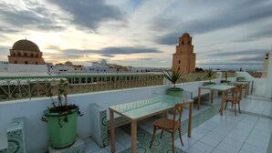 Terraço no telhado com mesa e cadeiras, plantas em vasos e vista para edifícios históricos.