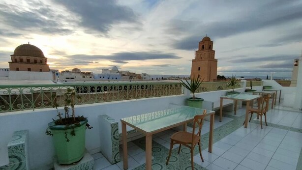 Una terraza en la azotea con mesa y sillas, plantas en macetas y vistas de edificios históricos.