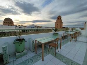 Una terraza en la azotea con mesa y sillas, plantas en macetas y vistas de edificios históricos.