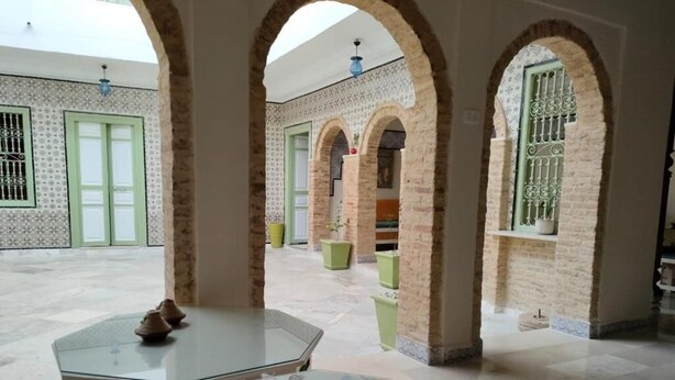 Pátio com mesa de vidro, um tecido vermelho e arcos de tijolo.