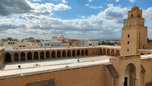Un patio con una torre, paseos con arcos y una estructura en forma de cúpula al fondo.