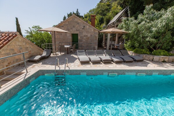 Ein Pool mit Liegestühlen und ein Steinhaus mit grüner Tür.