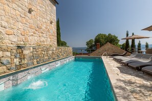 Ein Schwimmbecken mit Steinwänden, Liegestühlen und Sonnenschirmen.