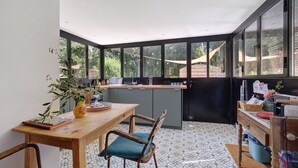 Una cocina con una mesa de madera, sillas, una planta en maceta y vistas amplias a través de grandes ventanales.