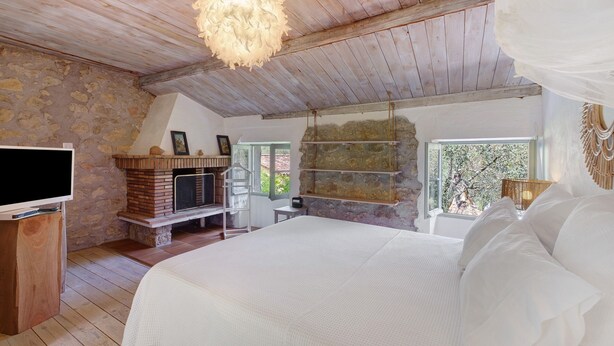 Un dormitorio con chimenea de piedra, una cama, un televisor y un ventanal grande.