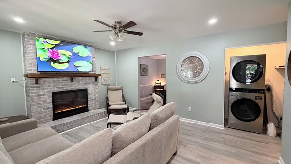 A living room with a fireplace, a TV, a ceiling fan, and a laundry area with a washing machine.