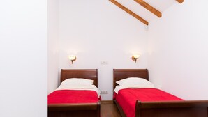 Ein Zimmer mit zwei Holzbetten, jeweils mit roter Bettdecke und weißen Kissen, unter einer schrägen Decke mit freiliegenden Balken.