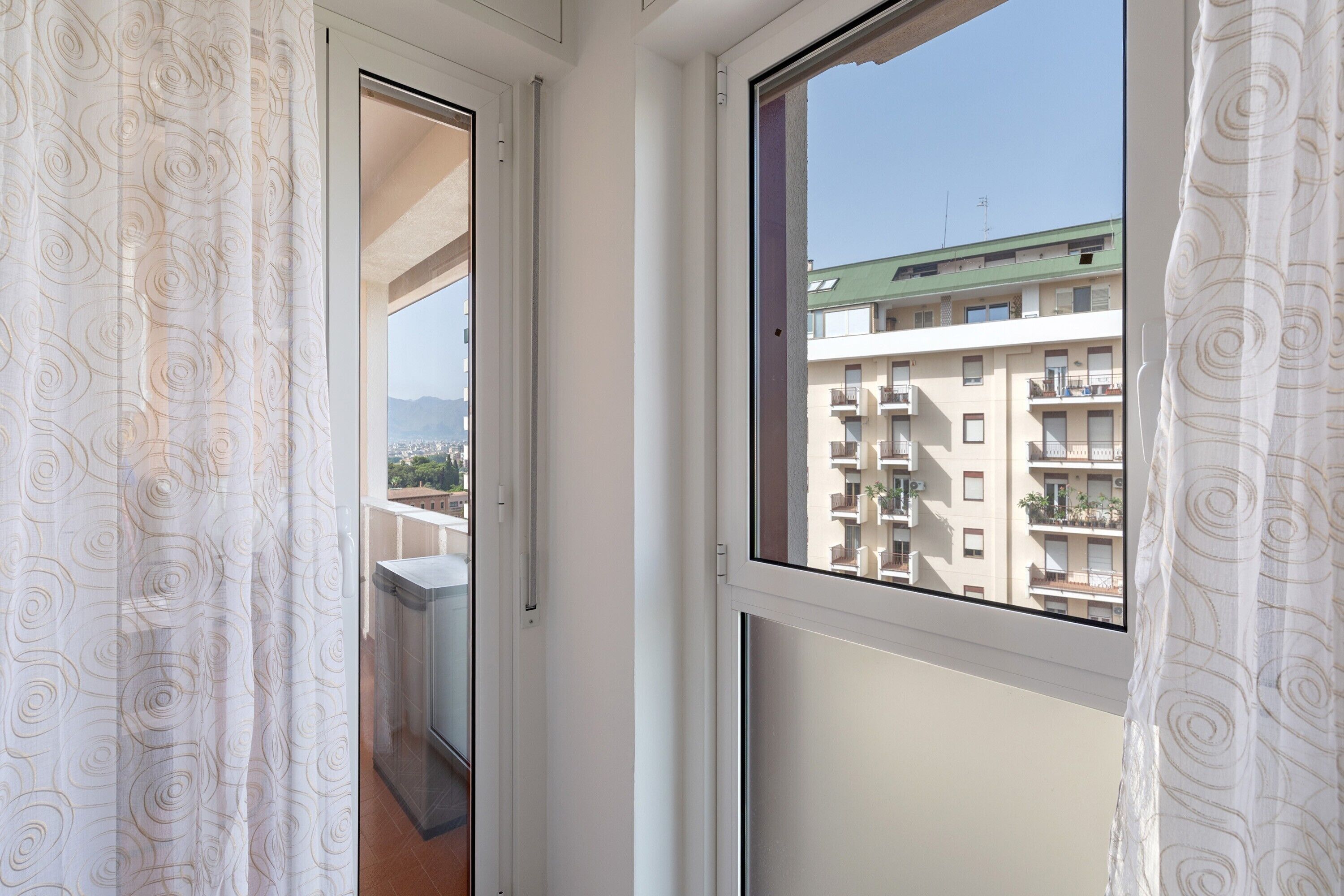 Una ventana con vista a un edificio de varios pisos y un cielo despejado.