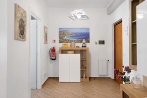 A hallway with a white door, a small white cabinet, a fire extinguisher, a painting of a coastal landscape, and a radiator. - 'Freedom House Palermo' Apartment with Mountain View, Wi-Fi and Air Conditioning (Palermo)