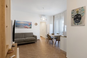 A modern living room with a grey sofa, a dining table with chairs, a TV, and artwork on the walls. - 'Freedom House Palermo' Apartment with Mountain View, Wi-Fi and Air Conditioning (Palermo)