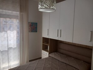 Ein Schlafzimmer mit Bett, Schrank, Pendelleuchte und einem Fenster mit Vorhängen.