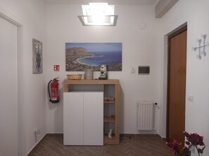 Ein Flur mit einem weißen Kleiderschrank, einem Gemälde einer Küstenstadt, einem Feuerlöscher, einem Heizkörper und einer Tür mit einem Kleiderhaken.