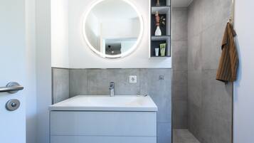 A modern bathroom with a white sink, a round mirror with lights, and a towel rack.