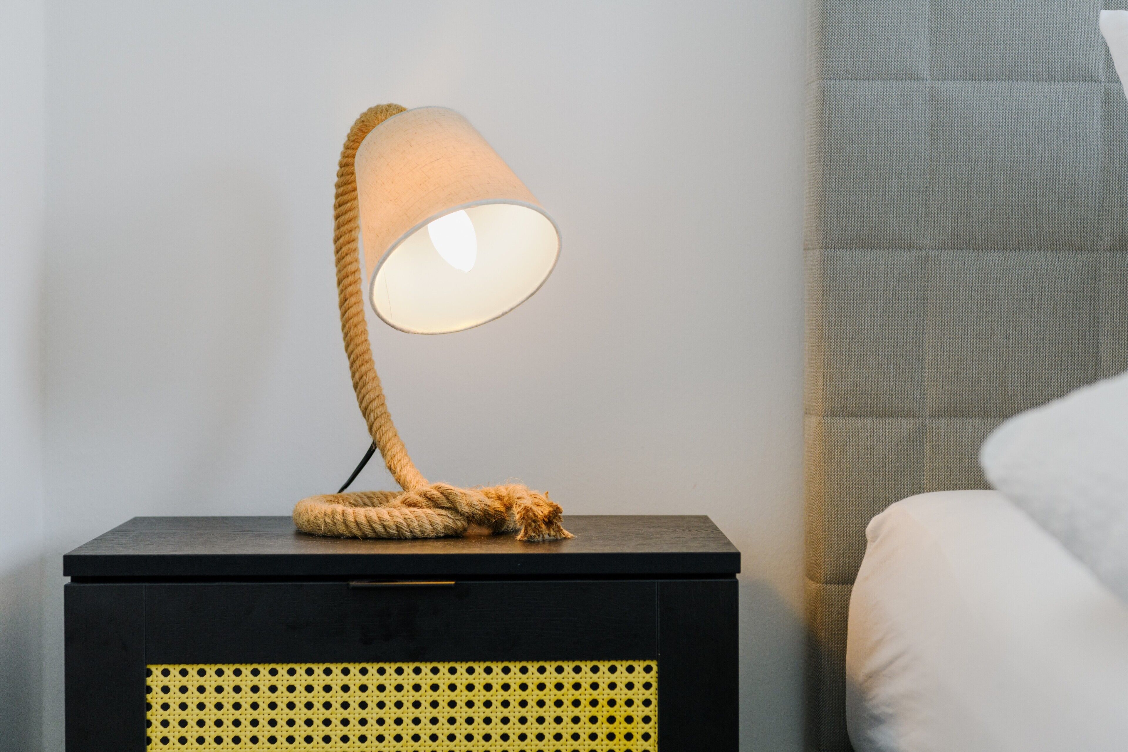 Eine Lampe mit Kordeldesign auf einem Nachttisch neben einem Bett.