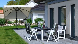 An outdoor patio with a table and chairs, a large umbrella, and a stone wall in the background. - Thatched Holiday Home 'Reetdachhus' in Klausdorf near Stralsund (Klausdorf)