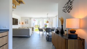 A modern living room with a sofa, dining table, chairs, and a kitchen area with wooden cabinets. - Thatched Holiday Home 'Reetdachhus' in Klausdorf near Stralsund (Klausdorf)