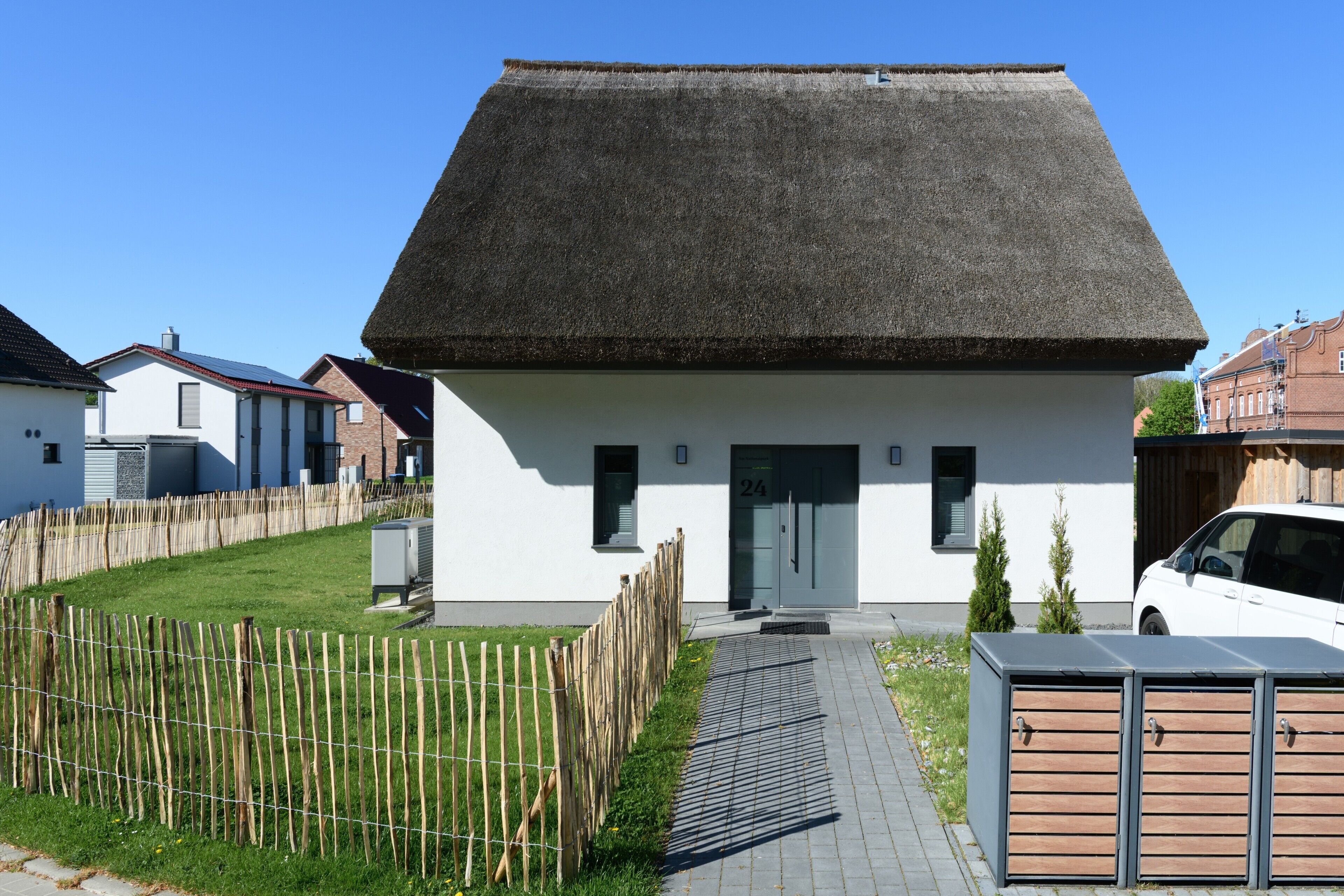 A modern house with a thatched roof, a paved driveway, and a fenced yard.