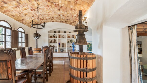 Zona pranzo con tavolo e sedie in legno, una botte grande e soffitto in mattoni.