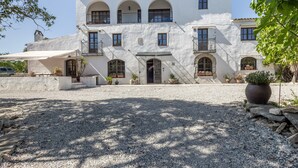 Un edificio a due piani con facciata bianca, diversi balconi e un vialetto sterrato.