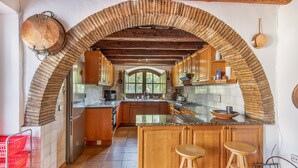 Una cucina con soffitto a volta in mattoni, pensili e basi in legno, un'isola centrale con sgabelli e una vista attraverso un'ampia finestra.