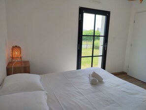 Et soveværelse med en seng, et natbord, en lampe og udsigt gennem et stort vindue.
