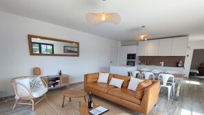 A modern living room with a brown leather sofa, a wicker chair, a round ottoman, and a dining area with white chairs. - Le 4 Pors Carn – walk to the beach, peaceful, sea view (Penmarch)