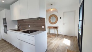 A modern kitchen with white cabinets, a wooden backsplash, and a built-in island with a sink. - Le 4 Pors Carn – walk to the beach, peaceful, sea view (Penmarch)