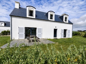Une maison à deux étages avec une terrasse en bois, un patio couvert et un jardin.