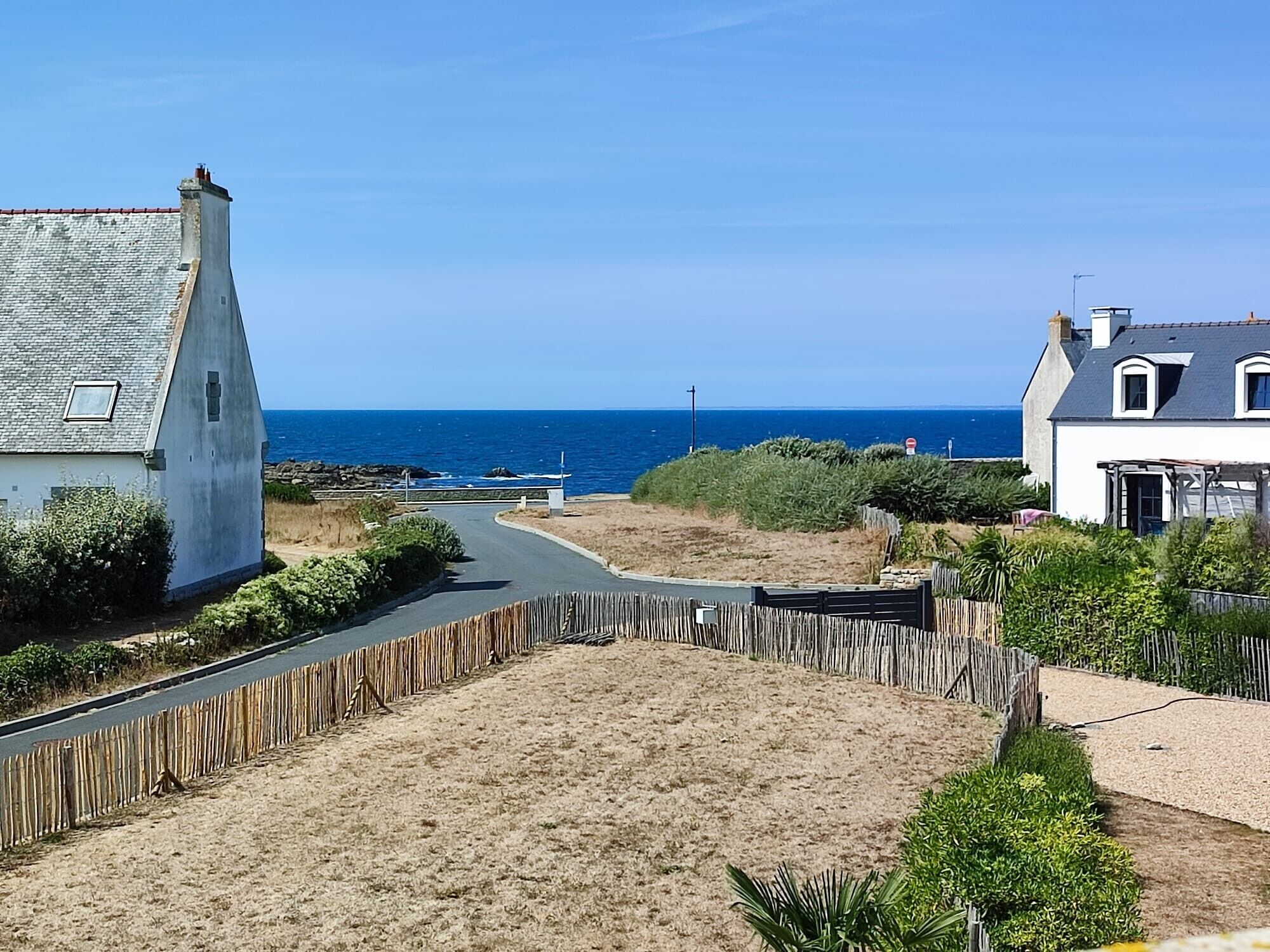 A coastal road with houses on either side, a sandy area in the middle, and the sea in the background.