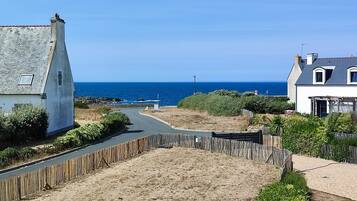 A coastal road with houses on either side, a sandy area in the middle, and the sea in the background.