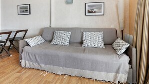 Una sala de estar moderna con un sofá gris, almohadones estampados, piso de madera y dos cuadros en la pared.