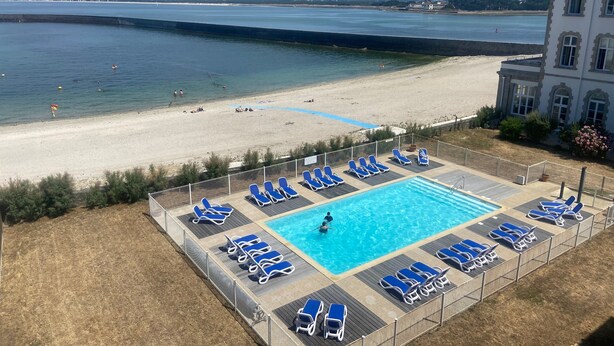 Zona de piscina con sillones, una alberca y vista a la playa.