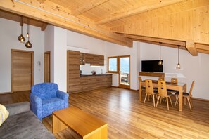 A spacious living area with a wooden ceiling, a sofa, a dining table with chairs, and a television. - Apartment “Zielspitze Residence Spisshof” with Mountain View, Shared Pool and Wi-Fi (Algund)
